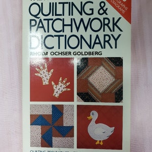May include: A book titled "The New Quilting & Patchwork Dictionary" by Rhoda Ochser Goldberg. The cover features a white background with the title in large black letters. It includes illustrations of quilting patterns and a duck. The book contains 1,745 photographs and diagrams.