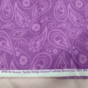 May include: Purple fabric with a white paisley pattern. The fabric has a corduroy texture. The text "CP40735 Persian Paisley, Springs Creative Products Group, LLC. 2011. Do not use for c" is printed on the bottom edge of the fabric.