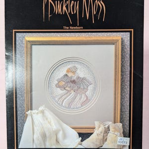 May include: A cross-stitch pattern featuring a mother holding a baby, with a white baby bonnet and booties. The pattern is titled "The Newborn" and is from Buckley Moss, Leaflet 110. The pattern is by June  Origio/Designs Inc.