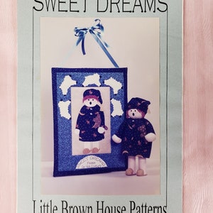 May include: A light blue paper with the text "SWEET DREAMS" and "Little Brown House Patterns". The image features a framed wall hanging and a doll, both with a night sky theme. The wall hanging and doll are wearing a dark blue outfit with stars.