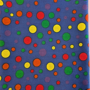May include: A blue fabric with a repeating pattern of colorful polka dots. The dots are in various sizes and colors, including red, yellow, green, orange, and purple. The fabric appears to be cotton or a similar material.