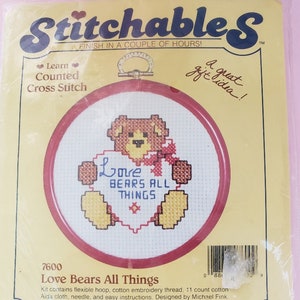 May include: A cross-stitch kit featuring a teddy bear holding a heart with the words "Love Bears All Things." The kit includes a flexible hoop, thread, Aida cloth, and needle. The packaging reads "Stitchable S" and "Finish in a couple of hours!"