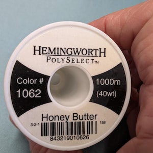 May include: A spool of Hemingworth Polyselect thread in Honey Butter color #1062. The spool contains 1000m (40wt) of thread. The label includes a barcode and the number 158.