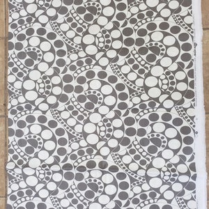 May include: A fabric with a repeating pattern of gray and white polka dots arranged in swirling, spiral-like designs. The fabric has a clean, crisp appearance, with a white selvage edge visible on the right side. The design is modern and geometric.