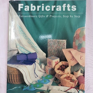 May include: A book titled "Fabricrafts" with the subtitle "50 Extraordinary Gifts & Projects, Step by Step." The cover is green with various craft projects, including felt fish, fabric-covered blocks, and small bags.