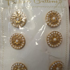 May include: Package of six vintage gold-tone buttons with white pearl-like accents. Each button features a central starburst design surrounded by a ring of small pearls. The package reads "UNUSUAL VALUE in Fashion Buttons."