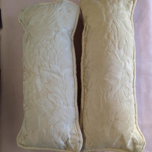 May include: Two off-white decorative pillows with a floral pattern. The pillows are rectangular and have a soft, plush texture.
