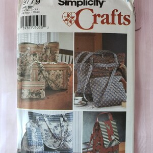 May include: Simplicity Crafts sewing pattern number 9779 for making four different bags. The pattern includes instructions for a tote bag, a smaller bag with a zipper, a backpack, and a smaller bag with a flap. The pattern is printed on white paper with a red heart logo and the words "Simplicity Crafts".