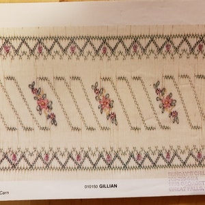 May include: A close-up of a white fabric with a green and pink embroidered design. The design features a repeating pattern of diagonal lines and small floral motifs. The fabric is numbered 1 through 11 on the left side. The text "010150 GILLIAN" is printed in the bottom right corner. The text "SUNDAY'S CHILD" is printed in the bottom right corner, along with a phone number, address, and city, state, and zip code.