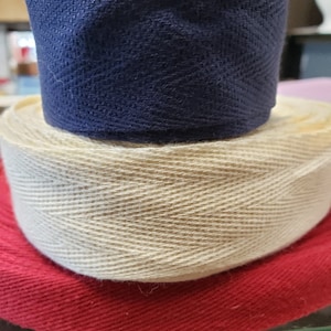 May include: Three rolls of fabric ribbon in different colors. The top roll is dark blue, the middle roll is beige, and the bottom roll is red.