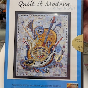 May include: A DVD case titled "Quilt it Modern" with Kathy McNeil. The cover features a colorful quilt design with musical instruments. The case is blue with text at the top and bottom, including "How should I quilt this?" and "Watch over Kathy's shoulder..."