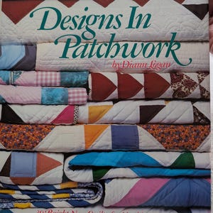 May include: A hardcover book titled Designs In Patchwork by Diann Logan, featuring a cover collage of various quilted fabric patterns in colors including blue, red, pink, orange, and white, with the subtitle 30 Bright New Quilts for Machine Piecing.