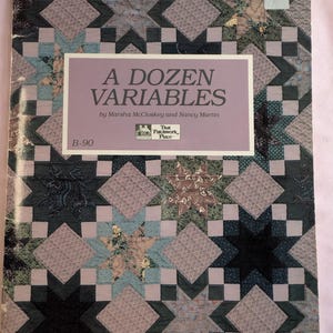 May include: A book titled "A Dozen Variables" by Marsha McCloskey and Nancy Martin. The book cover features a patchwork quilt design with a variety of colors and patterns.