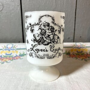May include: White ceramic cup with a black and white design of two cherubs and the text "Lover's Cup".