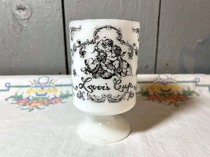 May include: White ceramic cup with a black and white design of two cherubs and the text "Lover's Cup".