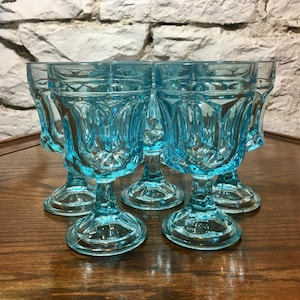 May include: Set of six light blue glass goblets with a fluted design. The goblets have a short stem and a round base.