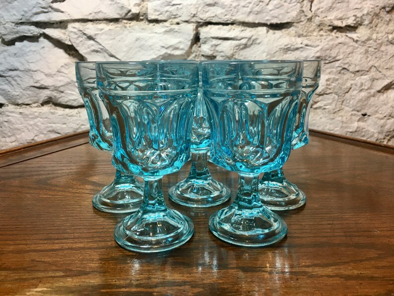 May include: Set of six light blue glass goblets with a fluted design. The goblets have a short stem and a round base.
