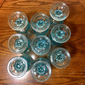 May include: A set of ten blue glass cups with a textured design. The cups are arranged in a circle on a wooden surface.