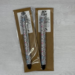 May include: Two black and white pens with a pink heart and bandage design. The pens are packaged in clear plastic and brown paper with the text "PEN CARE" and "PIN CARE" on the packaging.