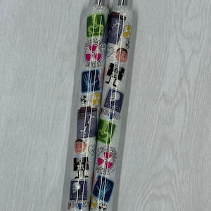 May include: Two white pens with black ink, featuring a glittery finish and colourful designs. The pens have a variety of images, including a skeleton, an x-ray, and the text "radiology squad".