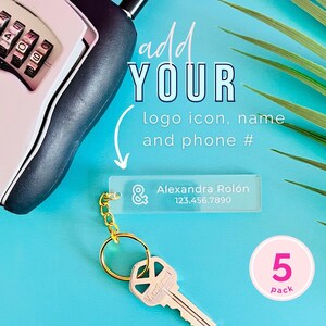 May include: A pack of five clear acrylic keychains with a gold chain and key ring. The keychain has a rectangular tag with an ampersand symbol and space for a logo, name, and phone number. The text "Alexandra Rolón 123.456.7890" is printed on the tag. The keychain is on a blue background with a green palm leaf.