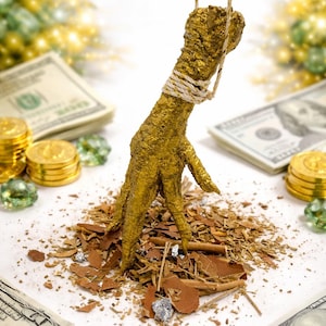 May include: A golden chicken foot sculpture suspended by a rope, resting on a bed of wood chips. The background includes stacks of US dollar bills, gold coins, and decorative green gems. The sculpture is a unique decorative item.