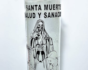 May include: A clear glass candle with a white wax interior. The candle features black graphics of a robed skeleton, an owl, and text that reads "SANTA MUERTE SALUD Y SANACION" and "HOLY DEATH HEALTH AND HEAL".