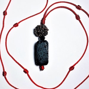 May include: A red cord necklace with a black rectangular pendant and a gold bead accent.