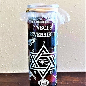 May include: A red glass candle with a white label that says "7 Veces Reversible". The label also features a white star of David with a black eye in the center and numbers 1 through 7 around the star. The candle is wrapped in clear plastic with a rubber band.