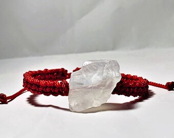 May include: A red braided bracelet with a clear, white crystal charm.