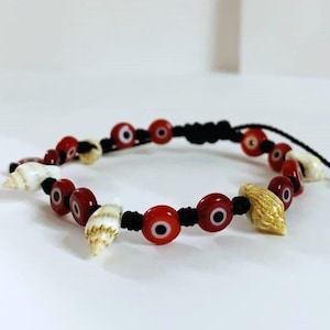 May include: A black string bracelet with red and blue evil eye beads and white and gold seashells.