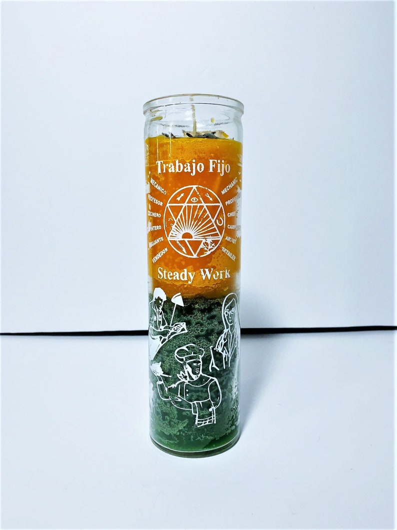 May include: A glass candle with layers of orange, green, and yellow wax. The candle has the words "Trabajo Fijo" and "Steady Work" printed on it, along with illustrations of various professions. The candle is designed to be used for spiritual or ritual purposes.