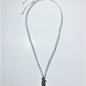 May include: A white braided cord necklace with a silver pendant of a skeleton figure holding a scythe.