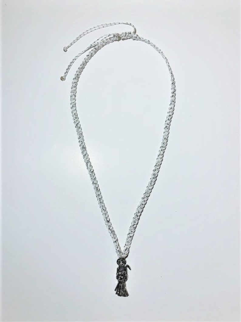 May include: A white braided cord necklace with a silver pendant of a skeleton figure holding a scythe.