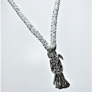 May include: A white braided cord necklace with a silver pendant featuring a skeletal figure holding a scythe.