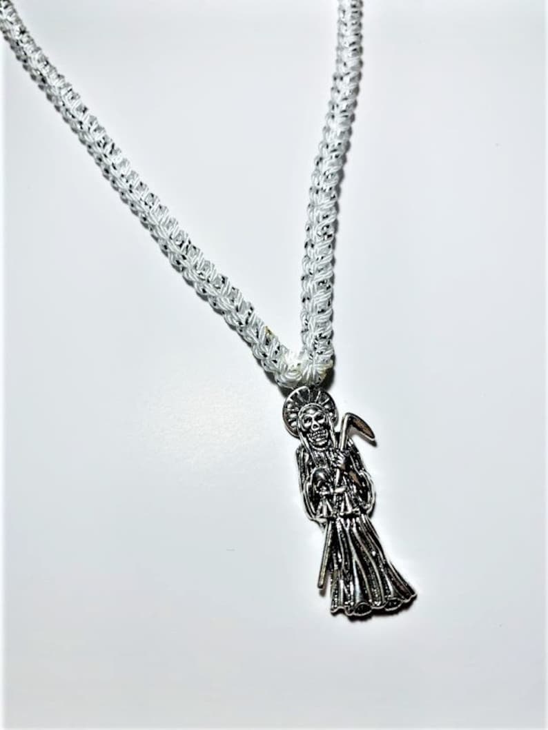 May include: A white braided cord necklace with a silver pendant featuring a skeletal figure holding a scythe.