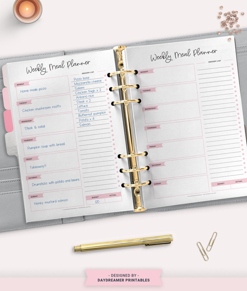 May include: A weekly meal planner with a grocery list and space to write in meals for each day of the week. The planner is open to a page with a list of groceries, including pizza base, mozzarella cheese, salami, chicken thigh, arborio rice, steak, lettuce, tomato, butternut pumpkin, potato, and salmon.