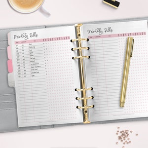 May include: A close-up of a gray and white planner with a pink polka dot pattern. The planner is open to a page titled "Monthly Bills" with columns for due date, amount, bill, and check boxes for each month of the year. The planner has a gold binder.