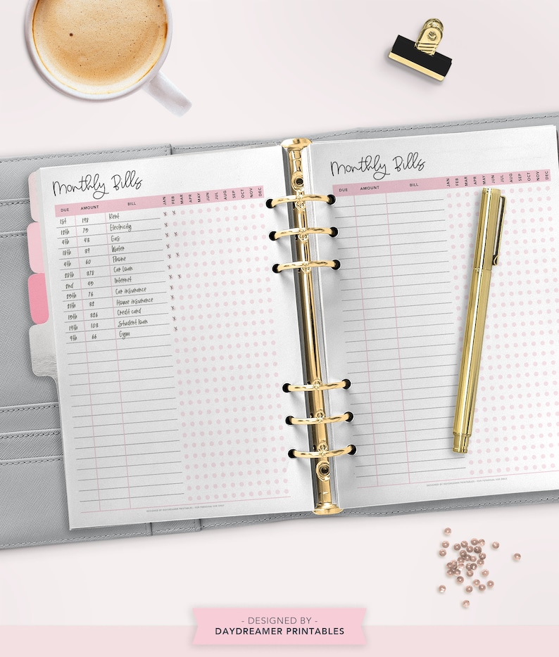 May include: A close-up of a gray and white planner with a pink polka dot pattern. The planner is open to a page titled "Monthly Bills" with columns for due date, amount, bill, and check boxes for each month of the year. The planner has a gold binder.