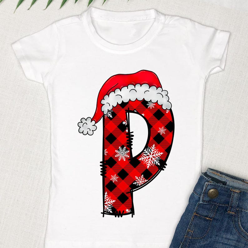 May include: White t-shirt with a red and black plaid letter "P" wearing a Santa hat. The letter is decorated with white snowflakes.