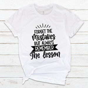 May include: White t-shirt with black text that reads "Forget the mistakes but always remember the lesson".