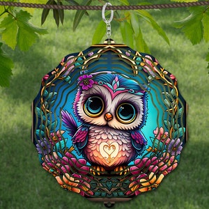 May include: A colorful metal wind spinner featuring a cartoon owl with large blue eyes and a pink heart on its chest. The owl is surrounded by flowers and leaves in shades of pink, purple, and green. The wind spinner is suspended from a metal ring.