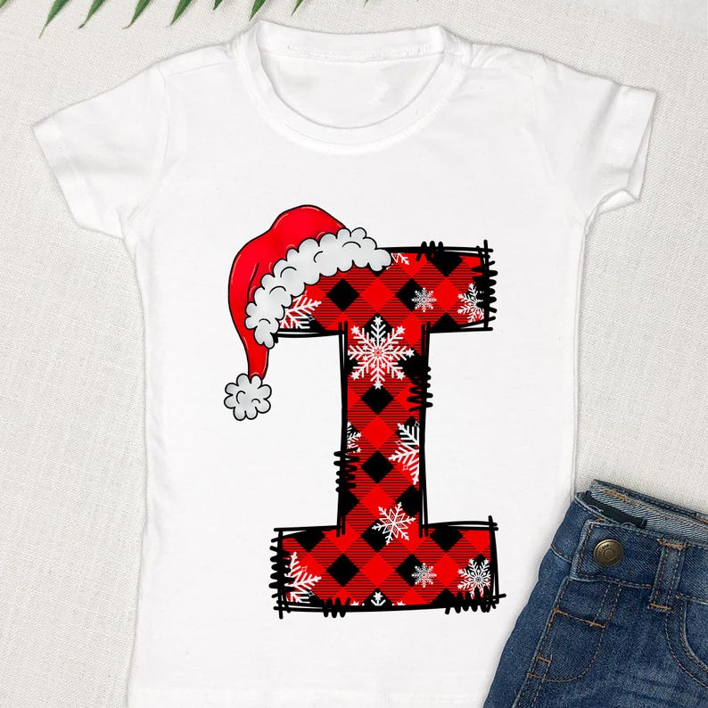 May include: White t-shirt with a red and black plaid letter I with a red Santa hat on top. The letter I is decorated with white snowflakes.