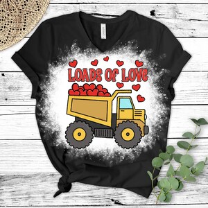 May include: A black t-shirt with a white bleach design of a yellow dump truck filled with red hearts. The text "Loads of Love" is above the truck.