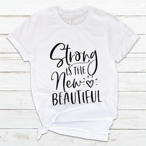 May include: White t-shirt with black text that reads "Strong is the New Beautiful" with a small heart symbol.