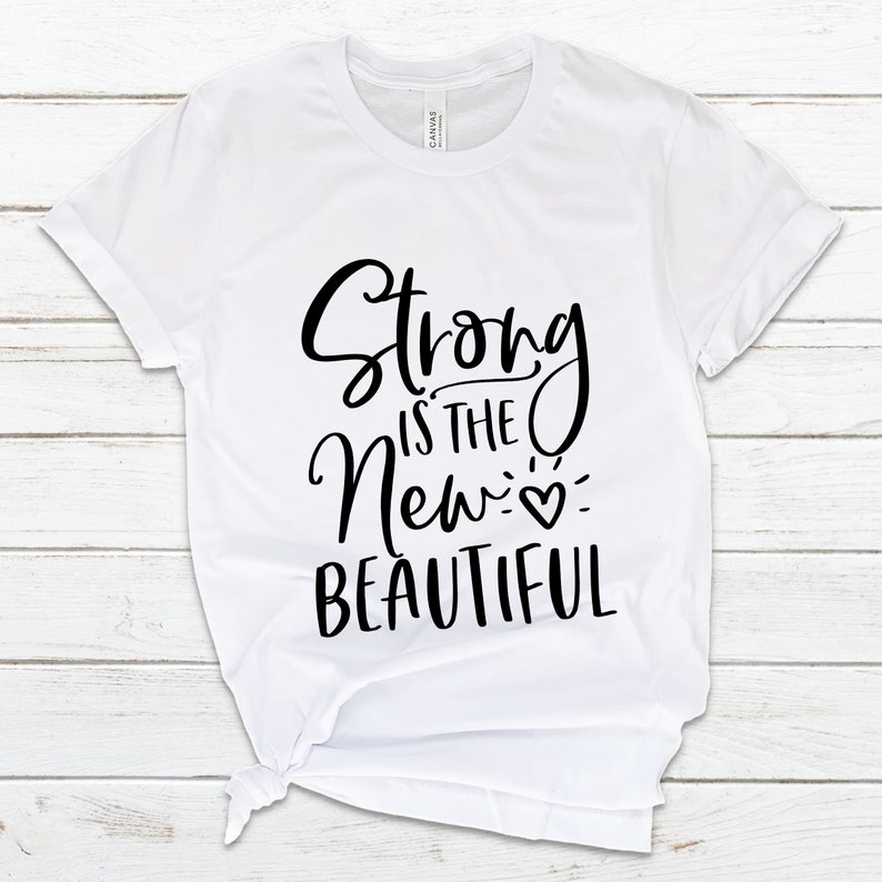 May include: White t-shirt with black text that reads "Strong is the New Beautiful" with a small heart symbol.