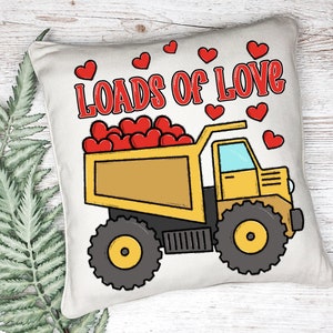 May include: A white pillow with a yellow dump truck carrying red hearts. The truck has the words "Loads of Love" printed on the pillow in red.