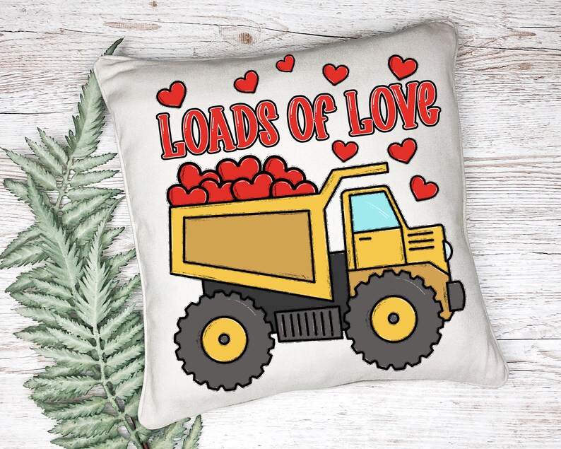 May include: A white pillow with a yellow dump truck carrying red hearts. The truck has the words "Loads of Love" printed on the pillow in red.