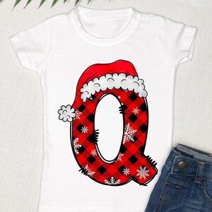 May include: White t-shirt with a red and black plaid letter Q wearing a Santa hat. The letter Q is decorated with white snowflakes.