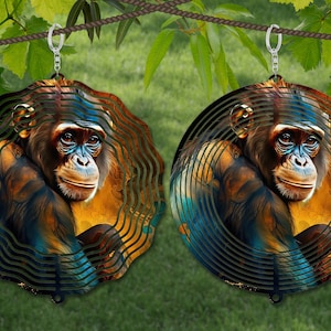May include: Two metal wind spinners with a colorful image of a chimpanzee. The spinners are hanging from a rope and have a swirling design.